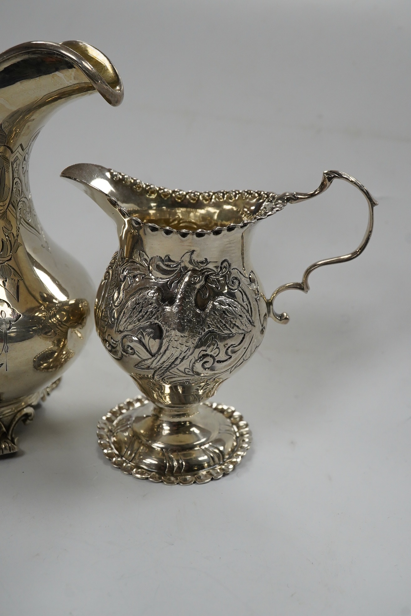 A Victorian engraved silver baluster cream jug, Henry Holland, London, 1862, 15cm, together with an Edwardian embossed silver cream jug, London, 1902, 10.5oz. Condition - poor